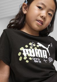 Čierne bavlnené tričko s výrazným bielym logom "PUMA" a textom "POĎME!!!", ozdobené svetlozelenými bodkami a grafickými návrhmi.