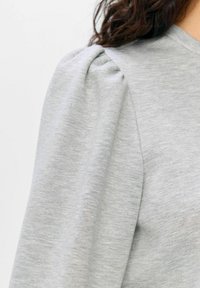 Grijze pullover met pofmouwen, gemaakt van zacht textuurstof. Heeft een relaxte pasvorm en subtiele stikdetails op de schouders.