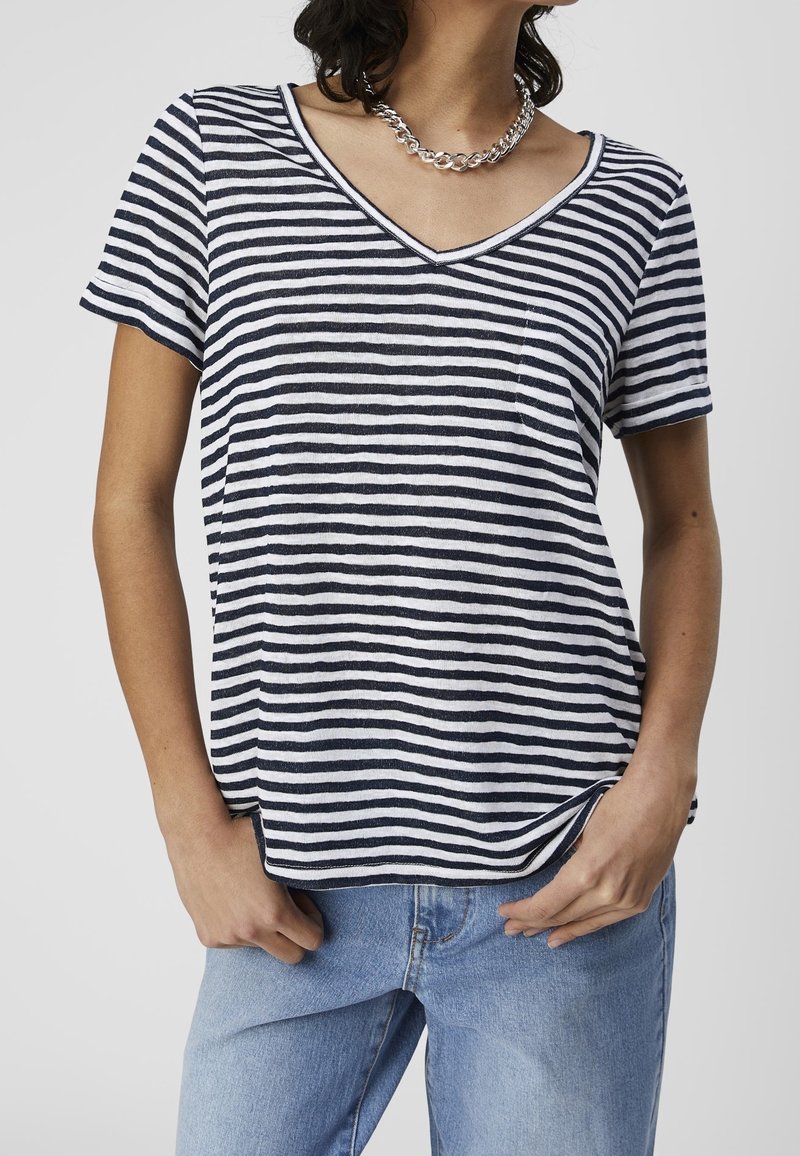 Femme portant un t-shirt rayé horizontal noir et blanc à col en V et manches courtes, et un jean bleu clair avec un collier chaîne argenté.