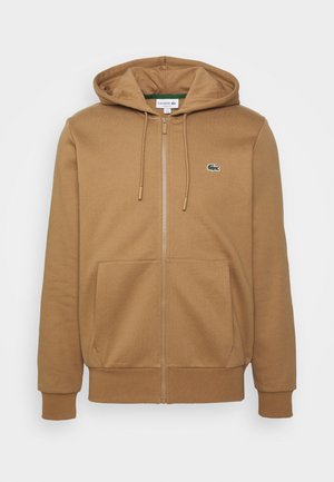 Felpa marrone con zip, cappuccio foderato, tasche frontali, polsini e orlo a coste. Presenta un piccolo logo di coccodrillo ricamato in verde.