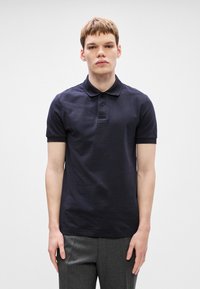 Μπλούζα πόλο σε ναυτικό χρώμα από μείγμα βαμβακιού με κοντά μανίκια, δύο κουμπιά και κεντημένο λογότυπο στο στήθος. Απαλή υφή, κανονική εφαρμογή.