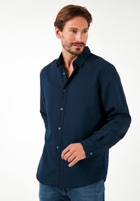 Camisa de botones azul marino con cuello clásico, bolsillo en el pecho y botones en contraste. Confeccionada en una tela suave y lisa.