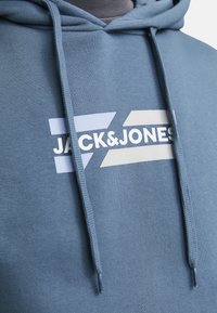 Light blue hoodie made of soft fabric, featuring a white logo "JACK&JONES" and graphic accents in lighter shades. Drawstrings at the hood.