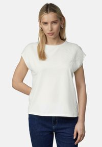 White short-sleeve shirt with a round neckline, featuring a subtle floral pattern on the left shoulder. Paired with dark blue jeans.