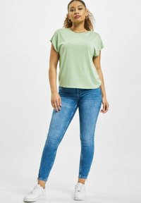 Lys grønn kortermet topp kombinert med blå skinny jeans og hvite joggesko. Toppen er glatt, og jeansene har en falmet tekstur.