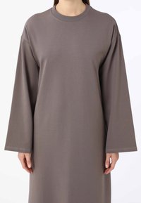 Robe grise à manches longues et col bateau. Tissu doux et extensible avec une coupe décontractée et des manches larges. Détails de couture minimaux en bas.