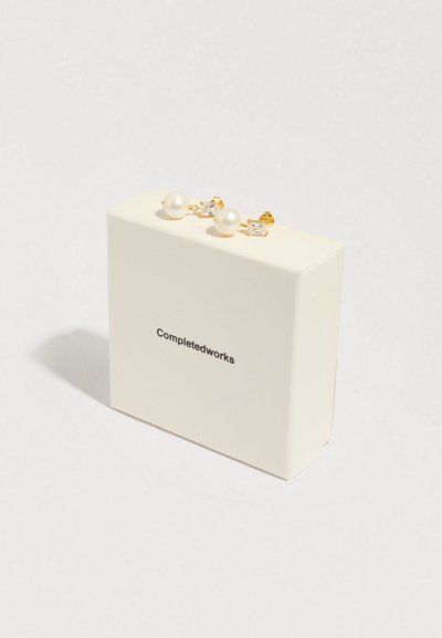 Brincos dourados com grandes pérolas brancas e cristais transparentes retangulares, apresentados numa caixa branca com a marca 'Completedworks'.