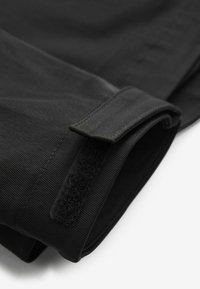 Material textil negru cu o textură netedă, dotat cu un închizător tip Velcro și detalii cusute. Materialul pare a fi durabil și ușor.