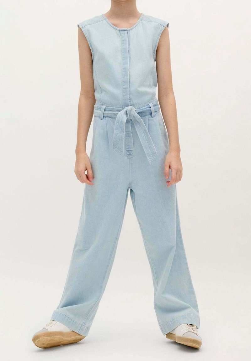 Combinaison en denim bleu clair sans manches, fermeture à boutons à l'avant et ceinture nouée à la taille. Caractérisée par une coupe large aux jambes et une texture douce.