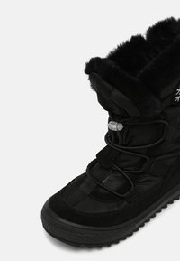 Botte noire imperméable avec une doublure en fourrure douce, une tige en textile, une semelle en caoutchouc saillante, et un système de laçage réglable pour un maintien sûr.