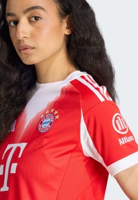 Punainen FC Bayern München -pelipaita, jossa on valkoisia yksityiskohtia, joukkueen logo, tähdet ja sponsorilogot. Valmistettu hengittävästä kankaasta, jossa on sileä rakenne.