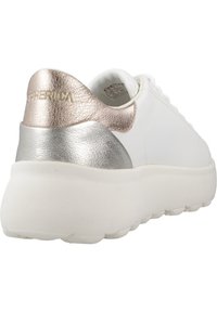 Sneaker blanc avec des accents métalliques bronze et argent au niveau du talon. Présente une surface lisse et texturée ainsi qu'une semelle épaisse et rembourrée.