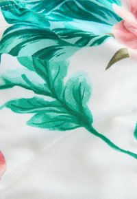 Țesătură florală cu frunze verzi și flori roz deschis pe un fundal alb, cu o textură fină și un contrast de culoare vibrant.