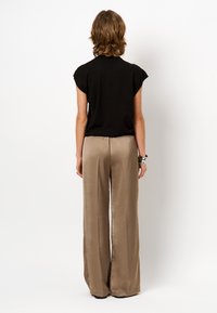 Zwarte korte mouwen top gecombineerd met beige wijde broek. Glad, glanzend materiaal met een ontspannen pasvorm, weergegeven vanuit de achterkant.