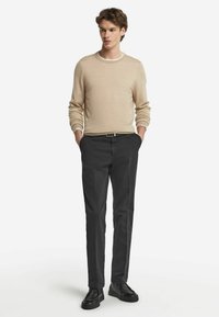 Beige rundhalsad tröja, lätt material, matchad med mörkgrå byxor. Svarta skor med texturerad yta. Enkel, modern design.