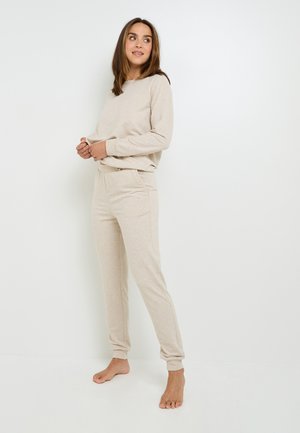 Completo loungewear beige realizzato in tessuto morbido, composto da una felpa con colletto a girocollo e pantaloni jogger affusolati con polsini elasticizzati e tasche laterali.