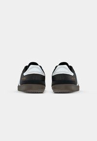 Black and white athletic shoes with a rounded toe, textured fabric, and rubber soles; features branding in gold on the outer side.