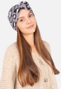 Bandeau en polaire douce, noir et gris à motifs, avec un design torsadé à l'avant. Porté avec un pull en tricot beige clair.
