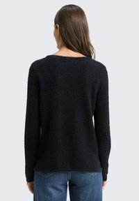 Black textured sweater with a round neckline and long sleeves, featuring a loose fit and a soft, fuzzy finish. Paired with blue jeans.