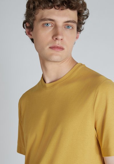 T-shirt di cotone giallo con scollatura rotonda e maniche corte. Il tessuto ha una texture liscia e un design aderente.