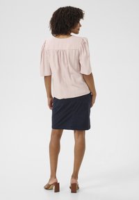 Blusa rosa pallido con maniche a sbuffo, abbinata a una gonna blu navy lungo il ginocchio. L'outfit presenta una vestibilità comoda e una morbida texture del tessuto.