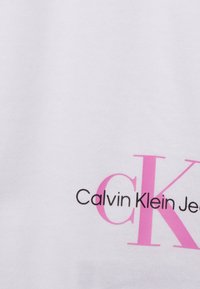 Biała bawełniana koszulka z logo "Calvin Klein Jeans" w czerni i różu. Prosty design z gładką teksturą i bez widocznych wzorów.