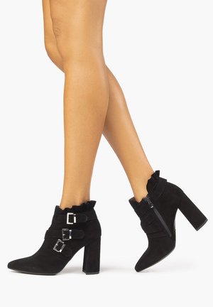 Black suede ankle boots with pointed toes, decorative buckles, ruffled collar, and block heels. Zipper on inner side for easy wear.