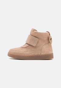 Beige suede ankle boots with a Velcro strap, round toe, and textured rubber sole. Notable loop detail on the heel.