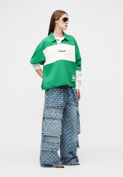 Femme portant un pull à manches longues vert et blanc, un jean cargo bleu oversize avec des poches, des sandales noires et des lunettes de soleil foncées.