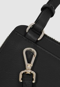 Angolo di borsa in pelle nera con dettagli in metallo color oro, chiusura con cerniera e superficie liscia con cuciture fini lungo i bordi.