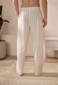 Pantalon de pyjama léger rayé en crème et beige, doté d'une ceinture élastique et de deux poches latérales, avec une coupe décontractée.