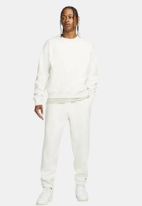 Weißer Pullover und passende Jogginghose aus weichem Stoff. Das Ensemble hat einen lässigen Schnitt und gerippte Bündchen. Weiße Sneakers vervollständigen den Look.