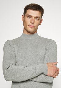 Light gray knit sweater with a high neck, ribbed cuffs, and smooth texture. Simple design with fitted silhouette and minimal detailing.