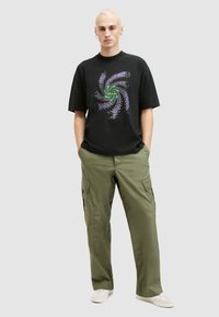 Svart grafisk t-shirt med en färgglad spiraldesign; ihop med gröna cargobyxor med sidfickor och en lös passform; avslappnat skovalt.