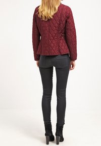 Bordeauxrode gewatteerde jas met een aansluitend model, voorzien van horizontale stiksels en een iets uitlopende onderkant. Gecombineerd met zwarte skinny jeans en laarzen.