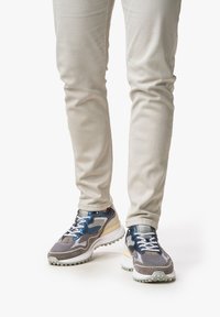 Harmaat ja laivansiniset verkko- ja mokkasneakerit, joissa on valkoinen kumipohja, monimutkainen ommel ja nauhat. Yhdistetty vaaleansävyisiin kapeisiin housuihin.