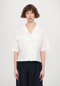 Witte blouse met korte mouwen, gemaakt van een gestructureerde stof, met kraag en knoopsluiting, voorzien van twee voorklauwen en trekkoorddetails.