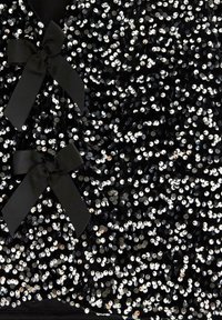 Černá látka zdobená stříbrnými flitry, se dvěma černými mašlemi. Textura je lesklá, s hustým, třpytivým vzorem po celé ploše.