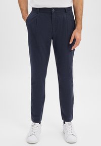 Granatowe spodnie o gładkiej fakturze, z przodu plisowane i zapinane na guzik. Połączone z białymi sneakersami dla casualowego wyglądu.