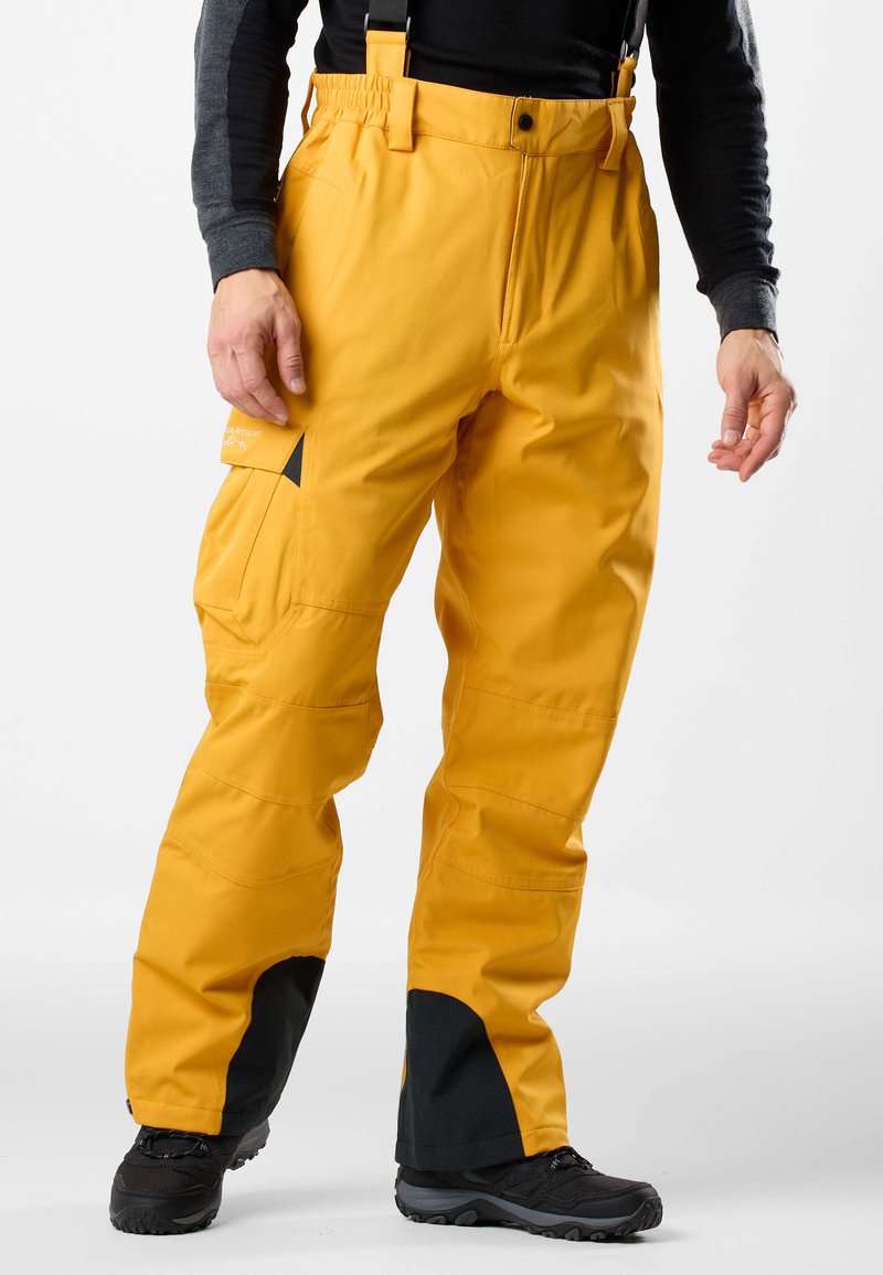 Żółte wodoodporne spodnie z regulowanymi szelkami, panelami na kolanach i boczną kieszenią z czarnymi akcentami przy mankietach.