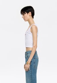 Witte geribbelde cropped tanktop met een ronde halslijn, gedragen met high-waisted blauwe spijkerbroek. Eenvoudig ontwerp, aansluitende silhouet, minimale details.