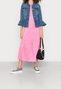 Giacca di jeans con maniche a volant, abito rosa con bottoni e gonna a balze, e sneakers con motivo. Borsa nera con accento a catena.