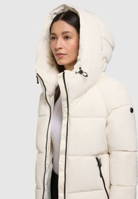 Weiße Daunenjacke mit großer Kapuze, schwarzen Reißverschlüssen und Seitentaschen. Das Material wirkt glatt und leicht glänzend und verfügt über gesteppte Abschnitte.