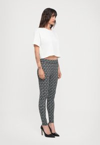 White cropped t-shirt, black leggings with repeating logo pattern, and black high-heeled shoes. Smooth textures and fitted design.