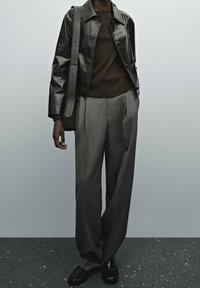 Black leather jacket, brown fitted shirt, grey wide-leg trousers, detailed with pleats. Black shoes, subtle stitching, minimalist design.