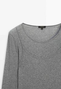 Chemise grise à manches longues en tissu doux et extensible. Présente un décolleté en scoop et une texture légèrement côtelée sans motifs ou accents distincts.