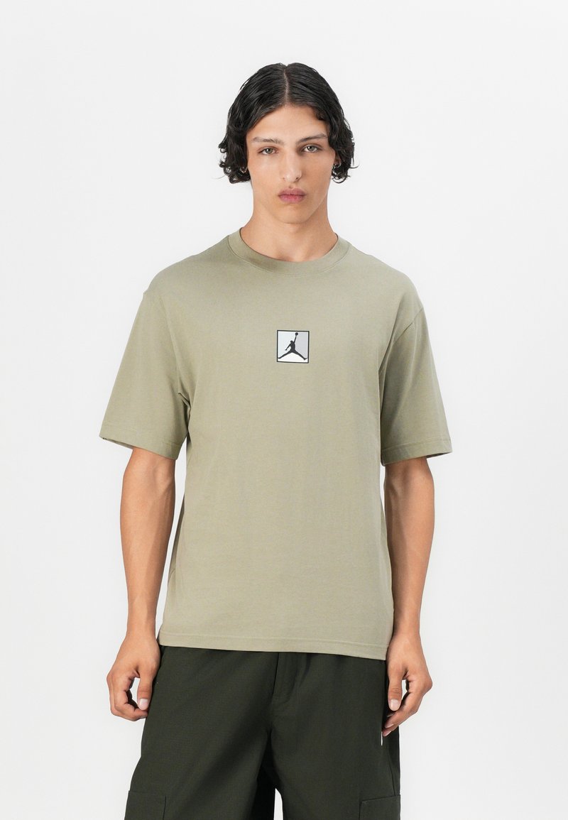 T-shirt en coton vert olive clair avec des manches courtes et un logo Jumpman noir dans un carré sur la poitrine. Texture lisse, col rond.