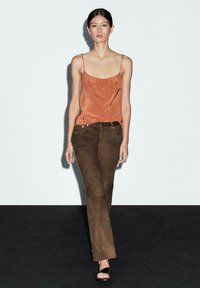 Rust-colored satin camisole with delicate straps paired with brown suede straight-leg pants and black leather sandals. Simple and modern design.