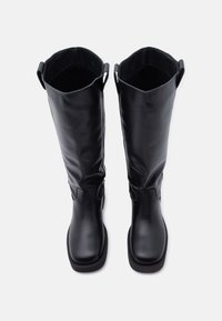 Μαύρες δερμάτινες μπότες έως το γόνατο με λεία υφή, στρογγυλεμένη μύτη και επίπεδη σόλα. Διαθέτουν δύο θηλιές στο πάνω μέρος για εύκολη φόρτωση.