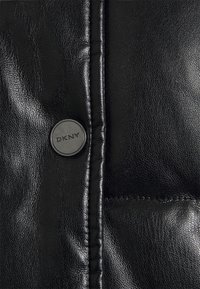 Svart läderjacka med en glansig yta, kviltat mönster och sömmar; inkluderar en rund svart DKNY-logoknapp.